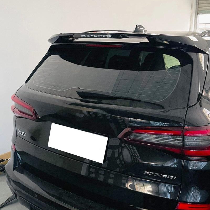 A black SUV rear view with a dark tinted rear window and a white license plate, photographed indoors against a plain light wall.